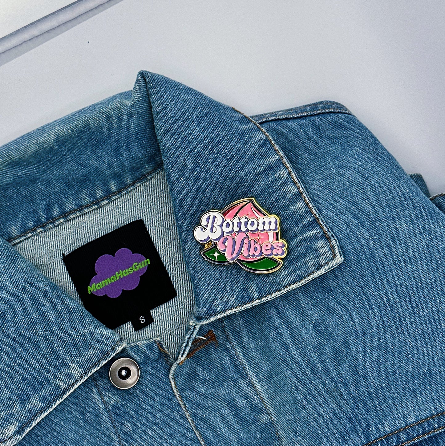 Bottom Vibes Enamel Pin with a big peach on the packground that has been pinned on a jacket.