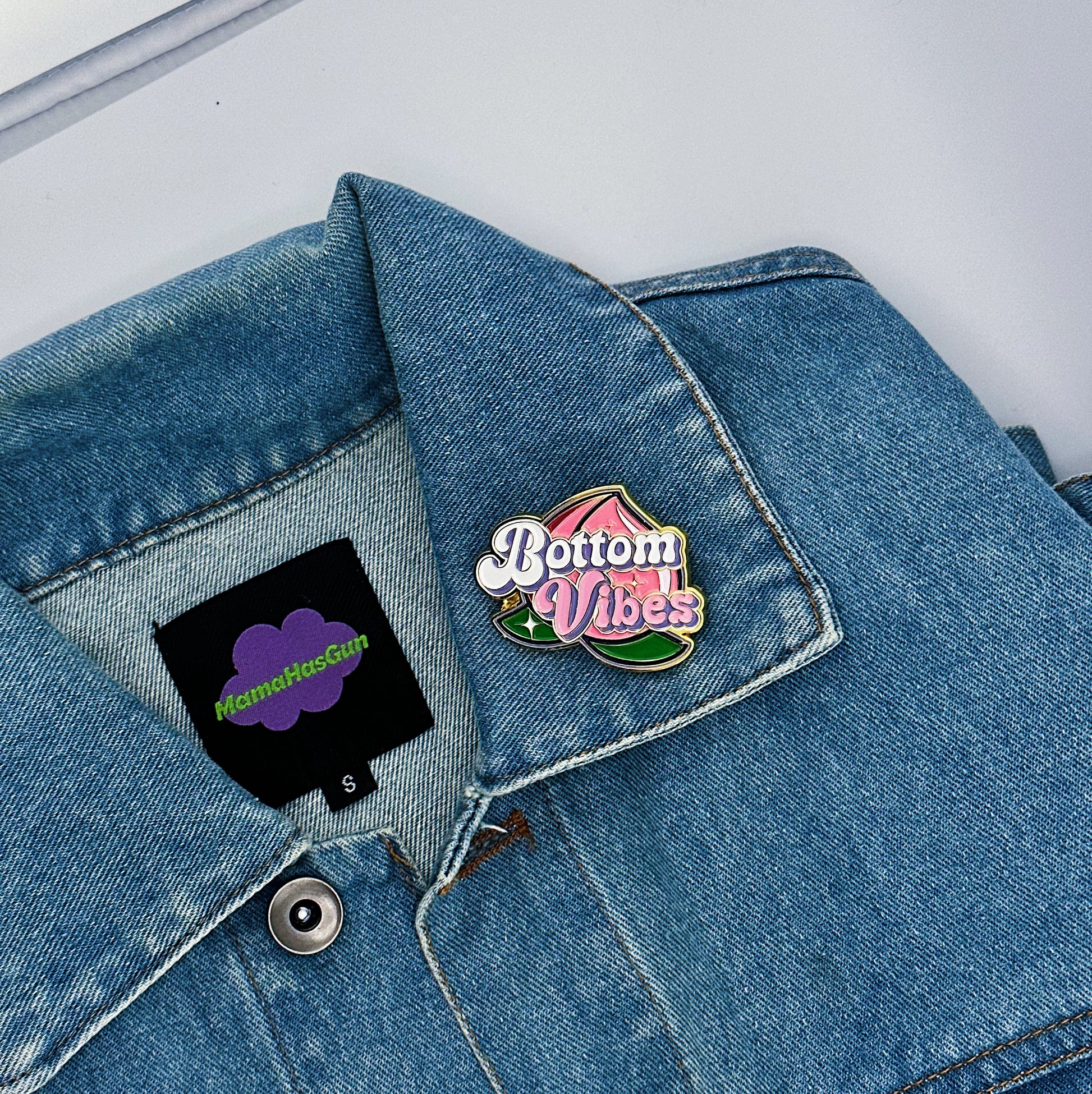 Bottom Vibes Enamel Pin with a big peach on the packground that has been pinned on a jacket.