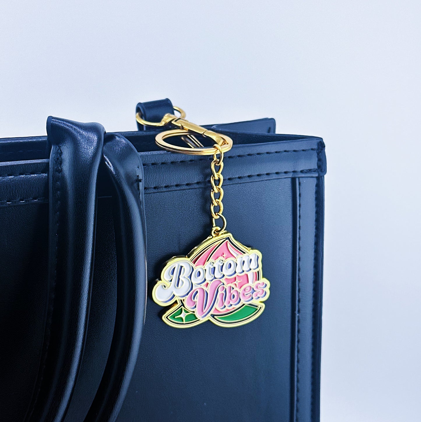 Key Chian has a bottom written in the middle and a big peach on the background, that has been placed on a hand bag.