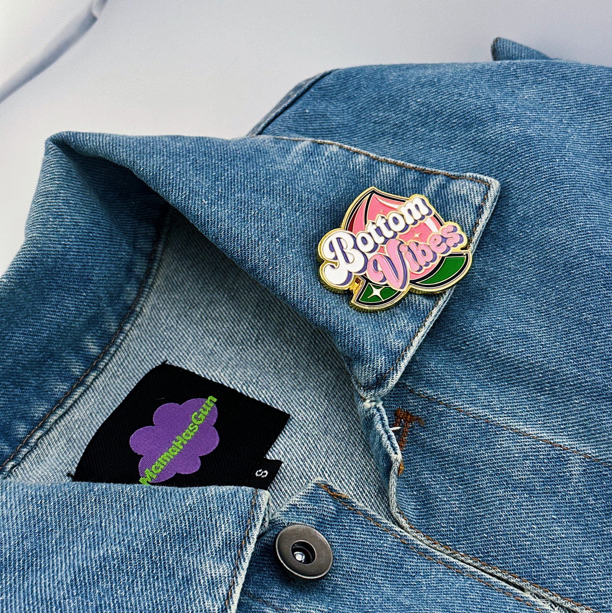 Bottom Vibes Enamel Pin with a big peach on the packground that has been pinned on a jacket.